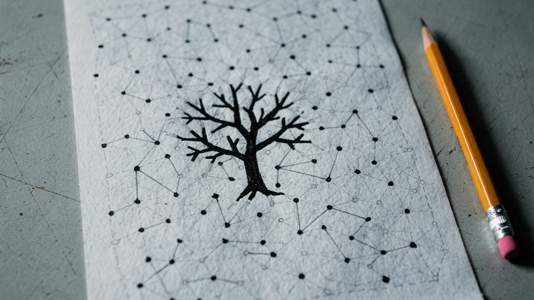 A hand-drawn network of dots and lines on paper, a bold ink drawing of a branching tree at its centre, a pencil beside it, under soft light.