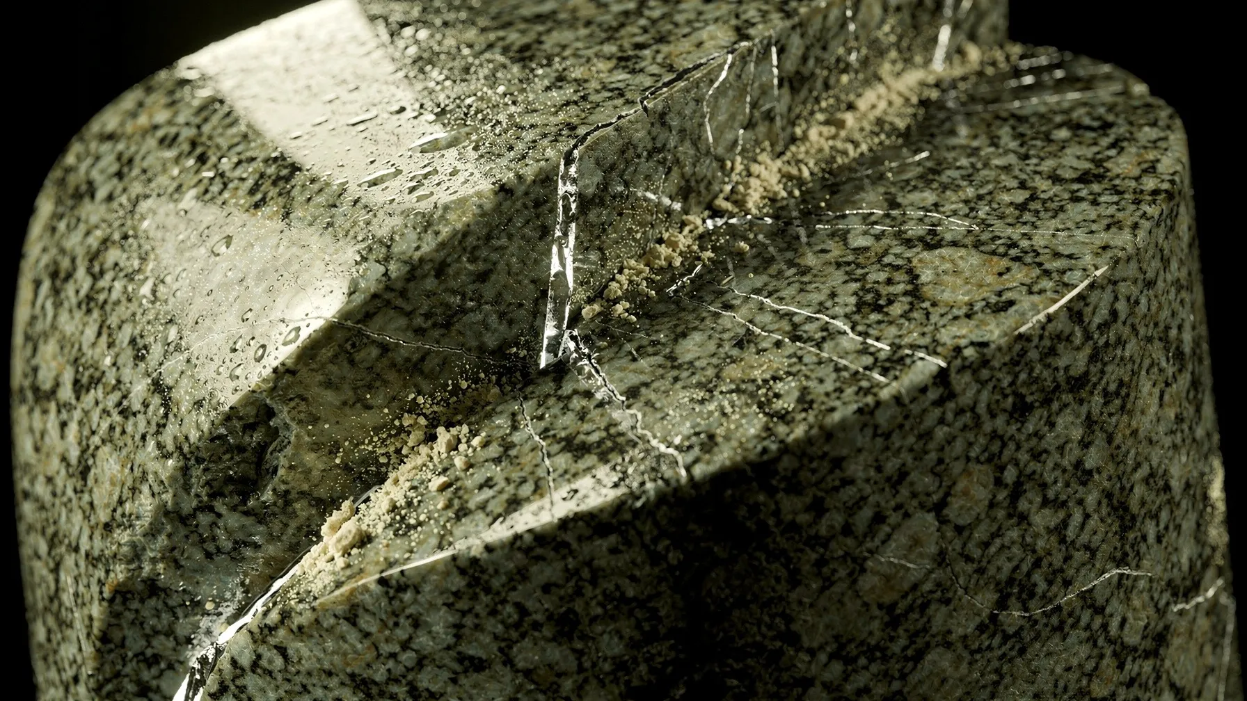 Macro photograph of a granite cylinder cut diagonally, the two halves offset along a thin wet fault line.