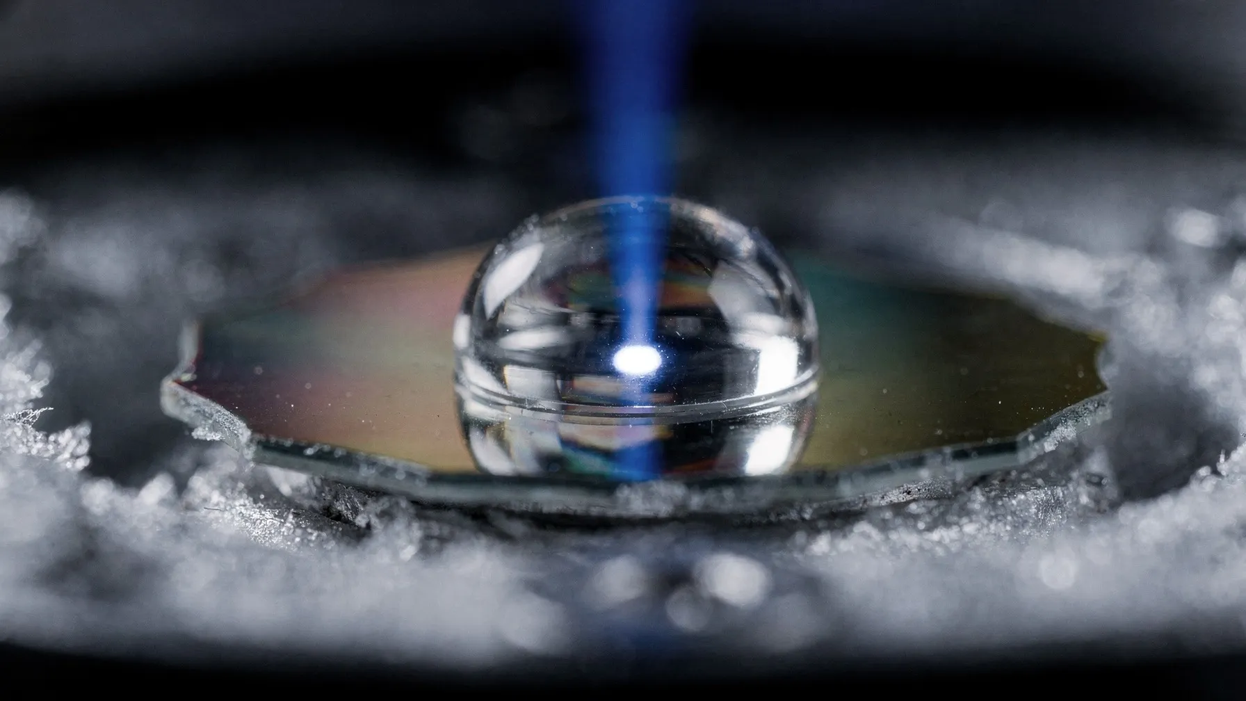 Macro photograph of a small glass hemisphere on a mirrored chip, a point of light at its base and a blue beam rising from it.